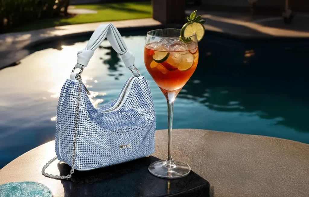 Bolso mini hobo Luna sobre mesa con cocktail y piscina de fondo.