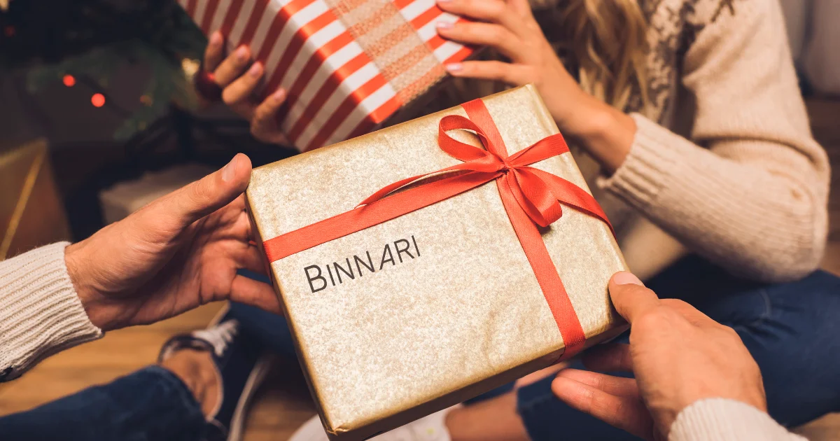 A man gives his partner a Christmas present with the Binnari handbags logo inscribed on it.